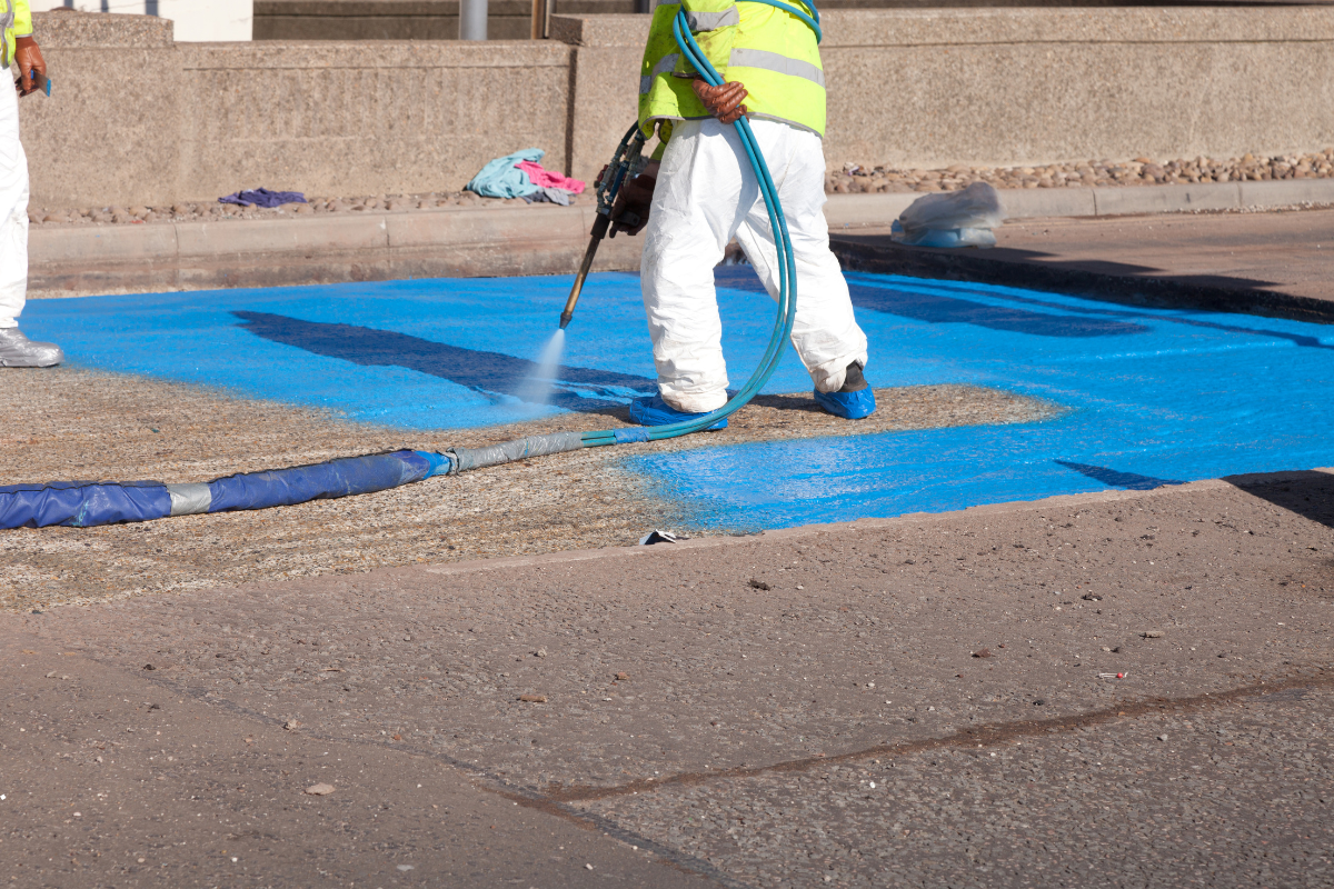 Worker applying flooring system with a spray machine