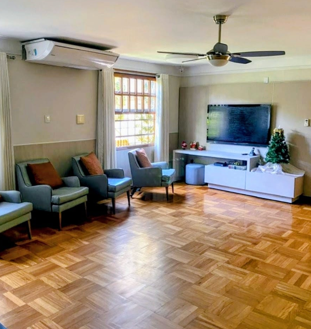 Sala de estar com piso de madeira, poltronas azuis, TV e ar condicionado.