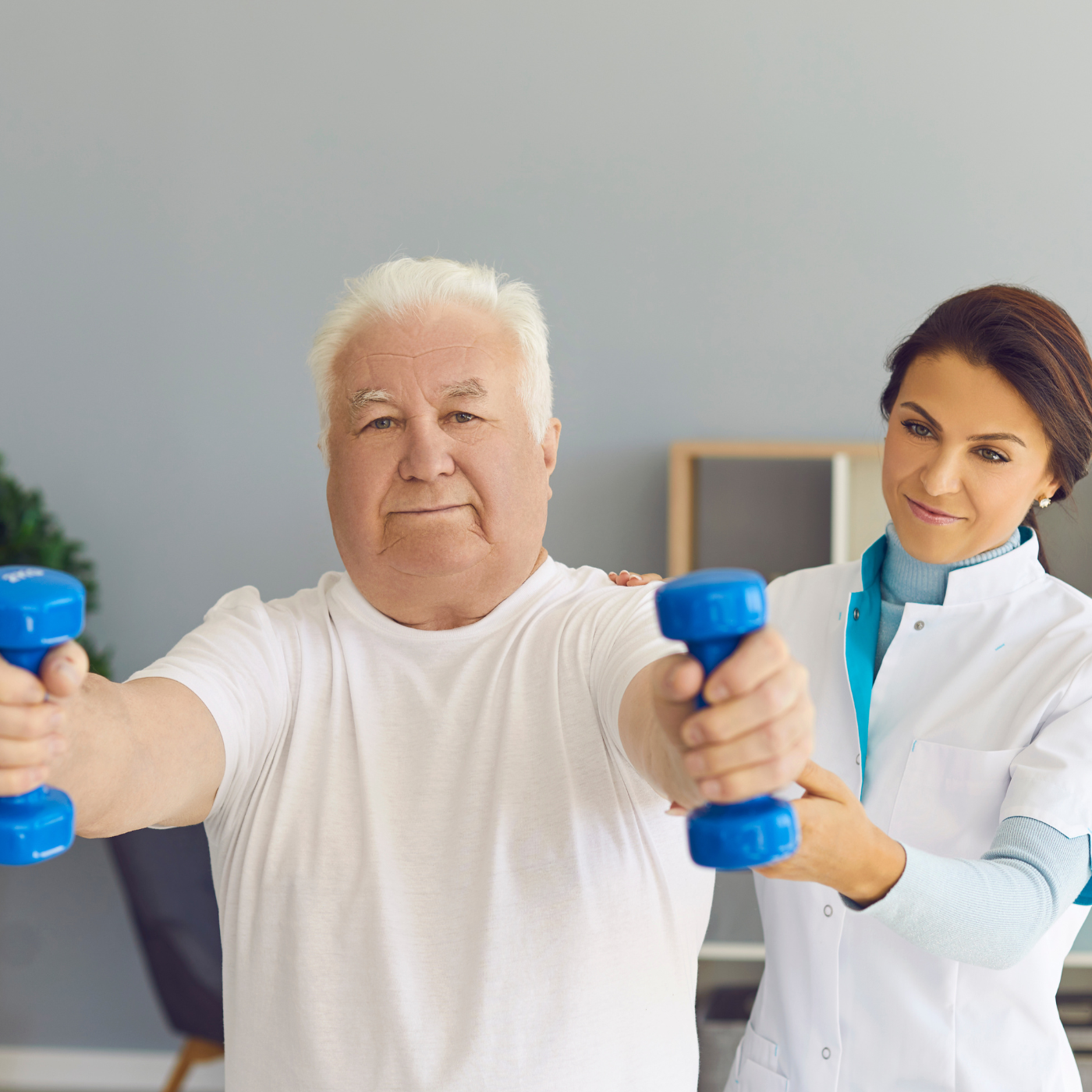 Homem levantando halteres azuis com a ajuda de um profissional de saúde em ambiente interno.