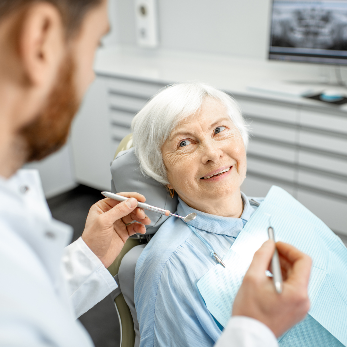 Dentista examinando os dentes de um paciente em um consultório odontológico. O paciente sorri enquanto usa um babador.