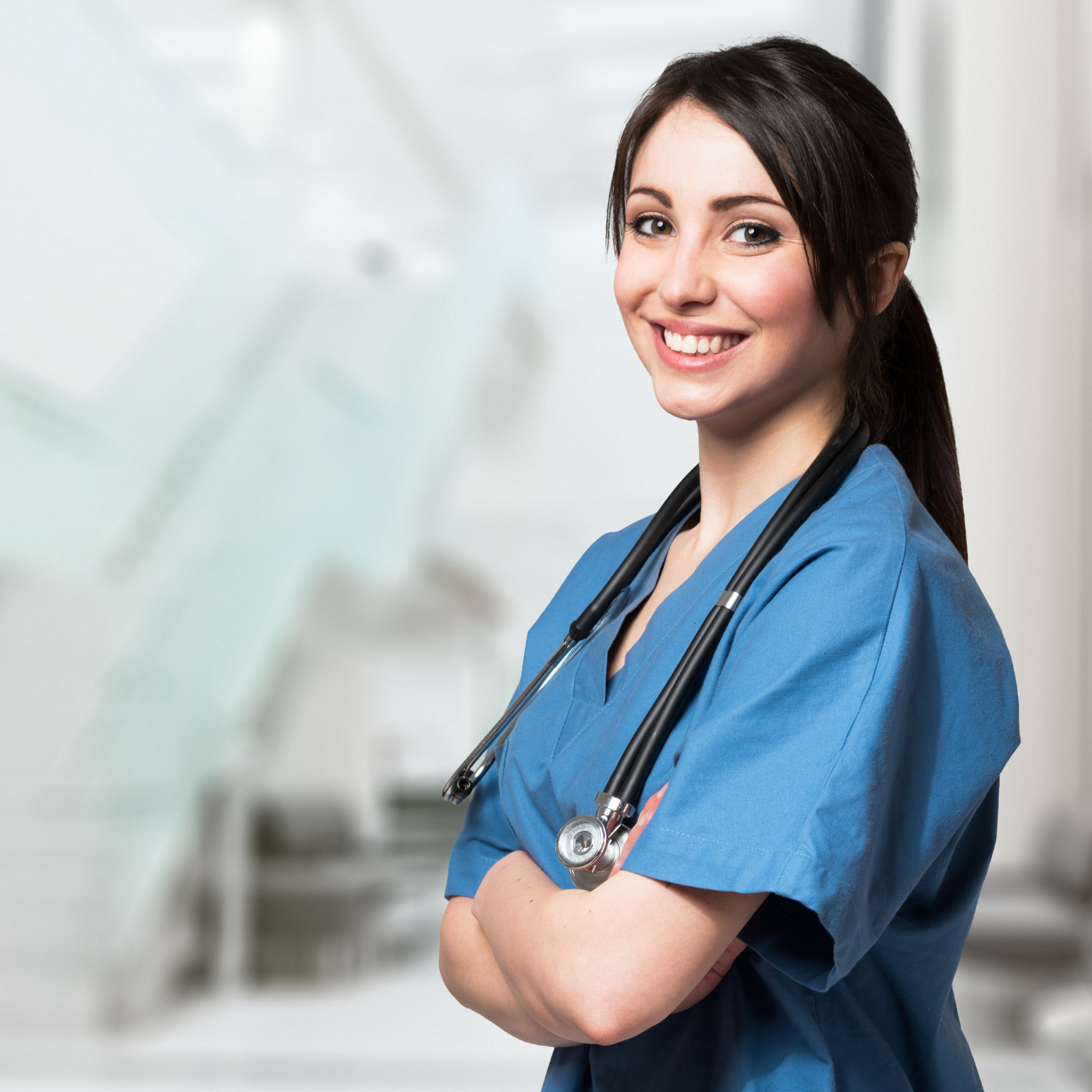 Enfermeira de uniforme azul com estetoscópio, sorrindo, braços cruzados em um ambiente médico.