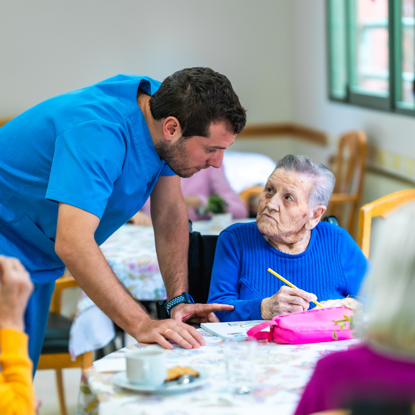 Cuidador auxilia um idoso com um quebra-cabeça em uma mesa, em ambiente interno.