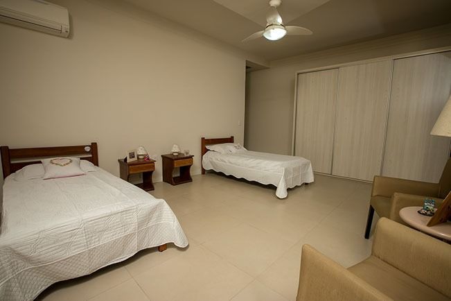 Dois quartos com camas de solteiro em tons claros, ventilador de teto, mesas de cabeceira e área de estar com poltronas.