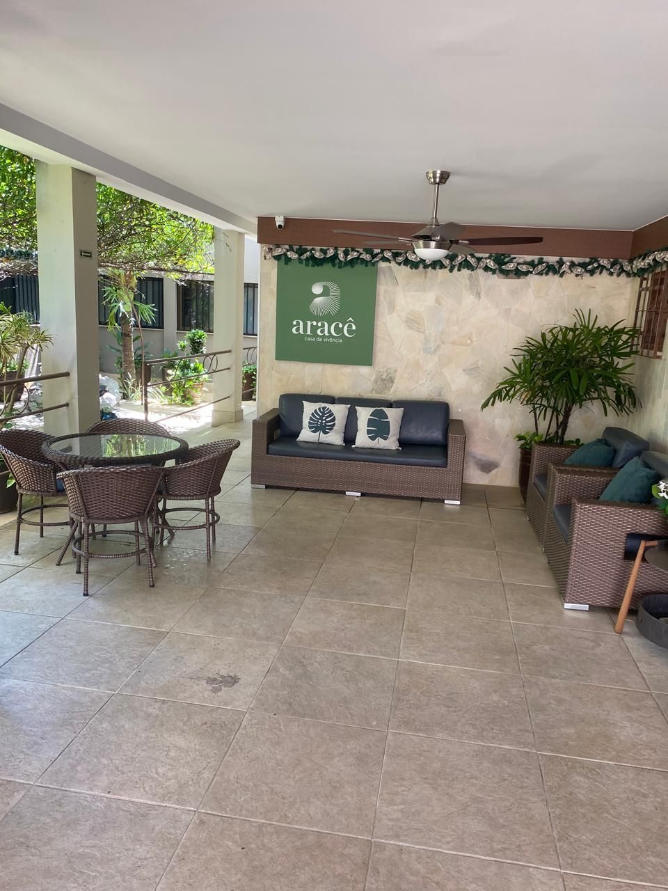 Área de estar externa coberta com móveis de vime e um logotipo na parede.