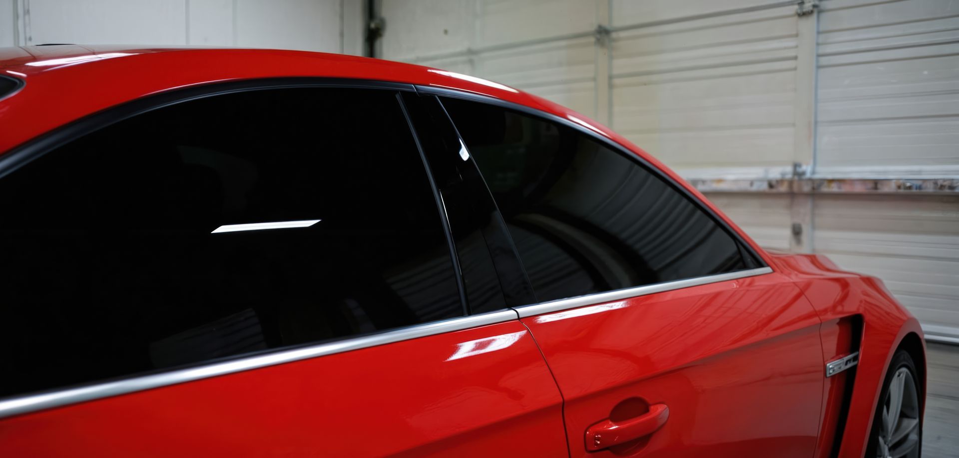 Red car with tinted windows in a garage setting.
