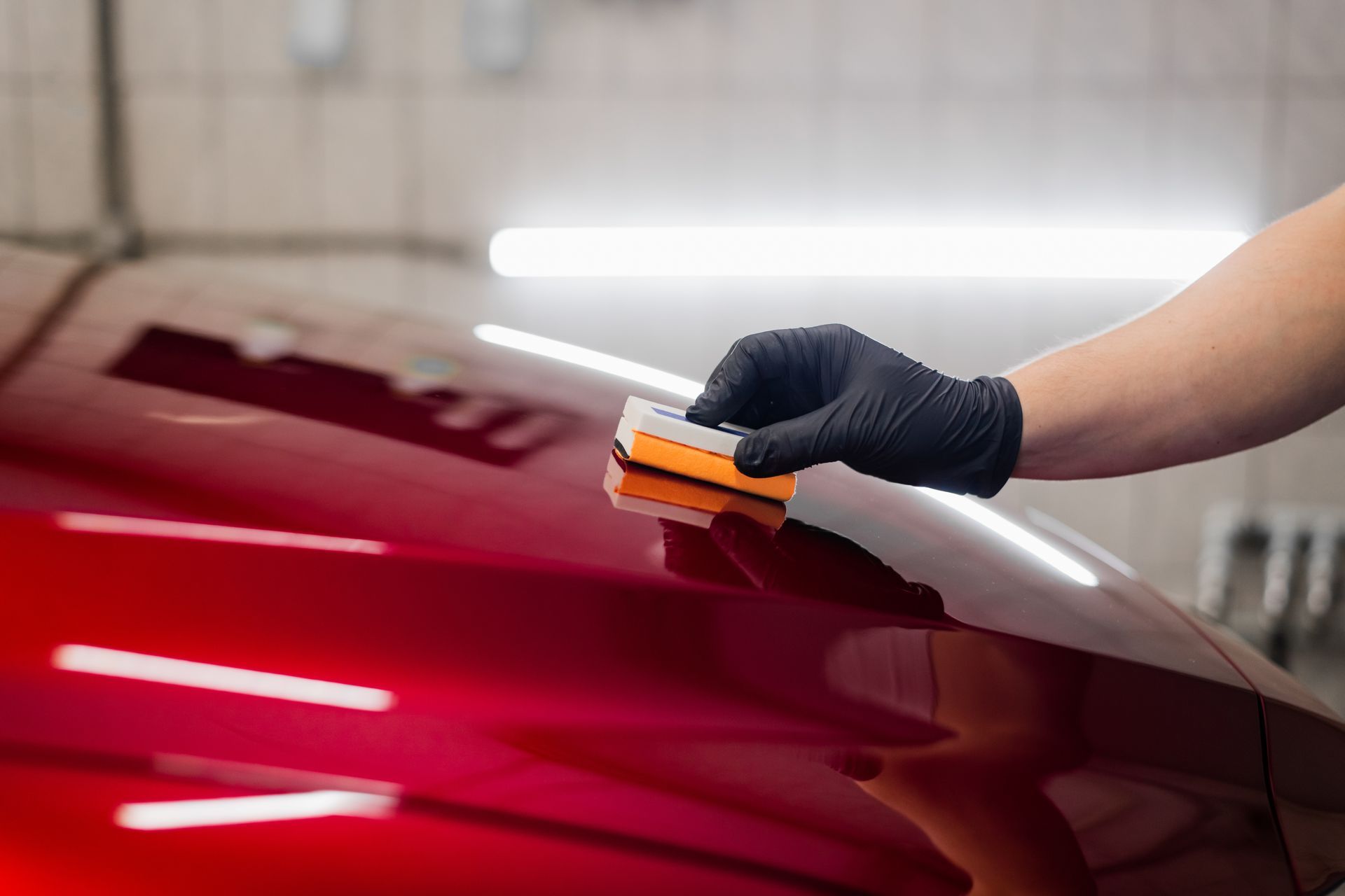 Person applying ceramic coating to a red car panel using an applicator.