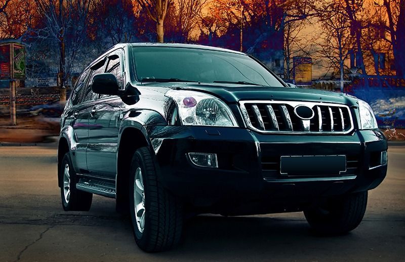 Black SUV parked on a road, with trees and buildings in the background.