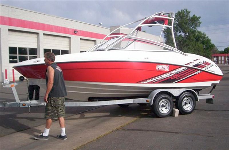 A person walks past a white and red recreational boat on a trailer parked in a lot.