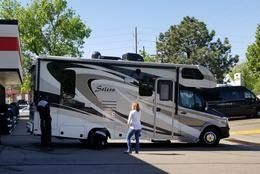A person stands looking at a large Solera recreational vehicle parked outdoors on a paved lot on a sunny day.