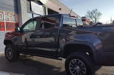 A dark gray crew cab pickup truck parked at an angle in front of a building with red and white storefront signage.