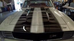 A white 1969 Chevrolet Camaro Z/28 with bold black racing stripes parked in an indoor garage.