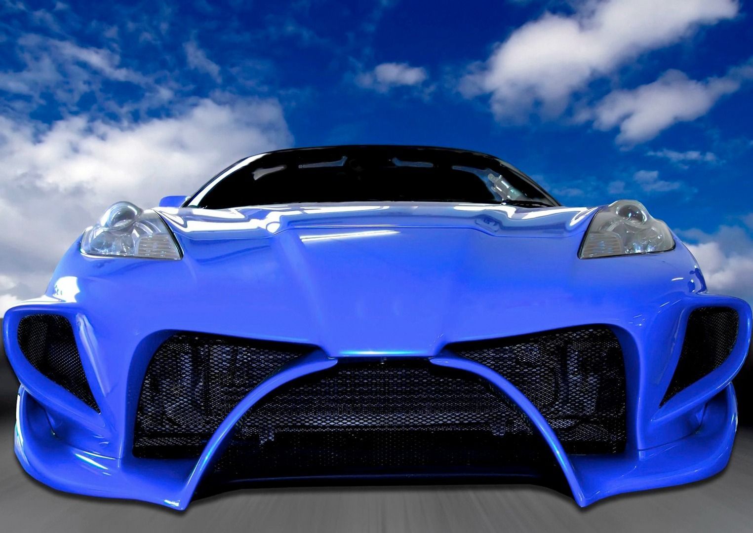 Blue sports car with custom front bumper, against a cloudy sky.