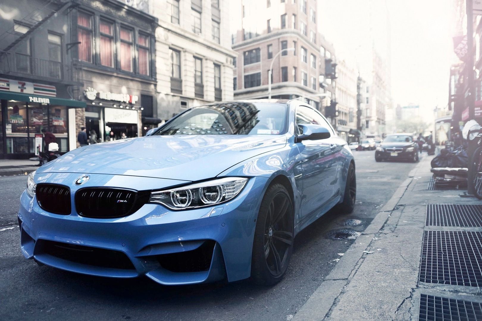 A light blue BMW sports car parked on a busy city street with tall buildings in the background.