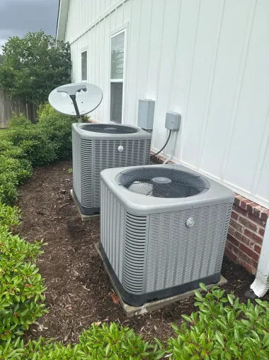 Two outdoor air conditioning units beside a white house, with a satellite dish nearby.