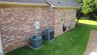 Side of a brick house with two air conditioning units and a grassy yard