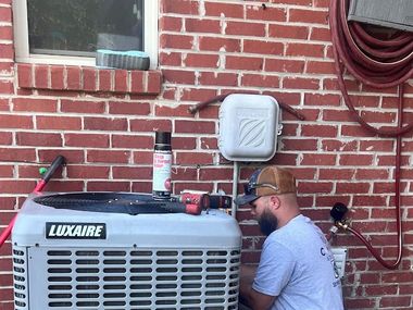 Technician inspecting outdoor Luxaire HVAC unit beside a brick wall