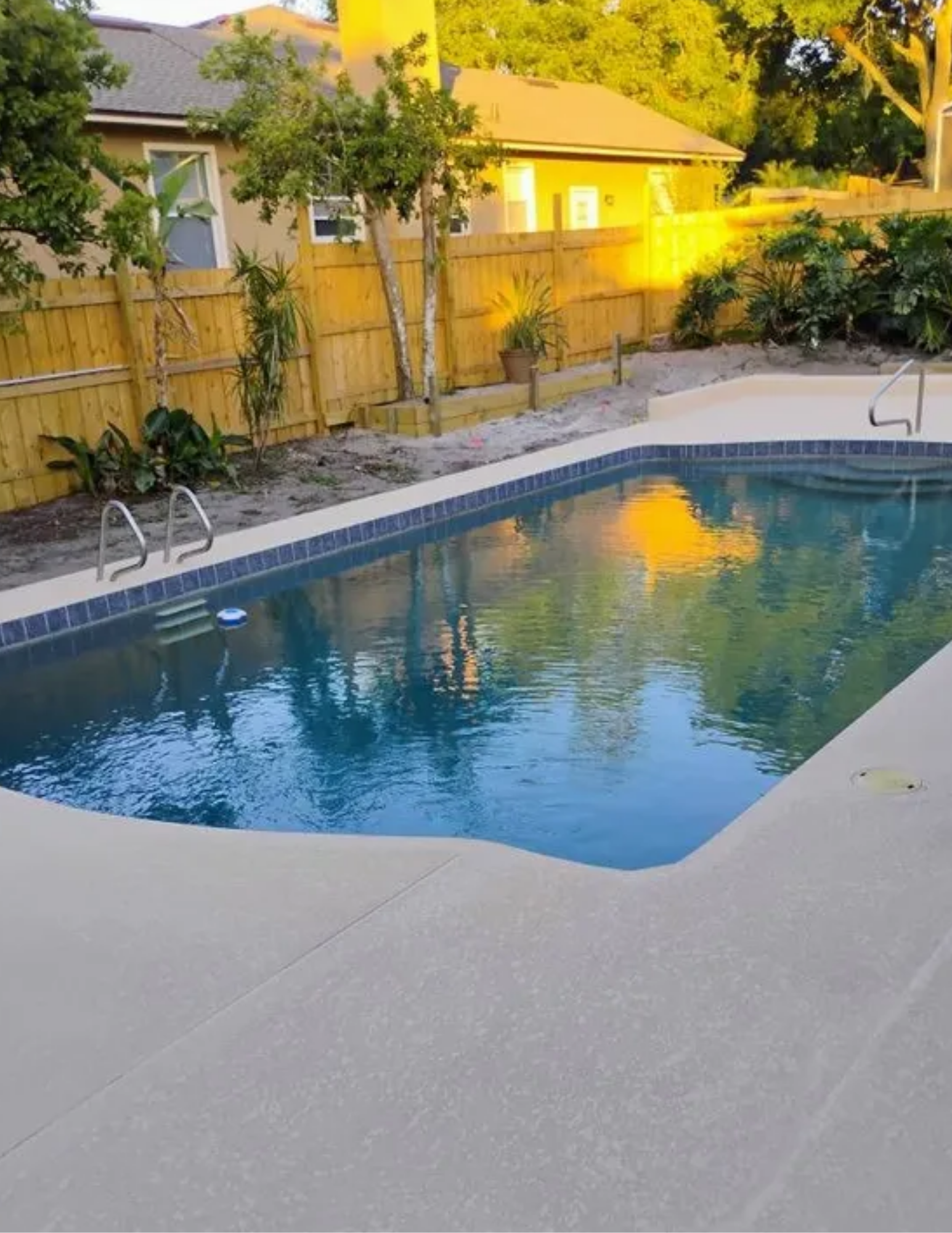 A cat excavator is sitting on the grass next to a body of water.