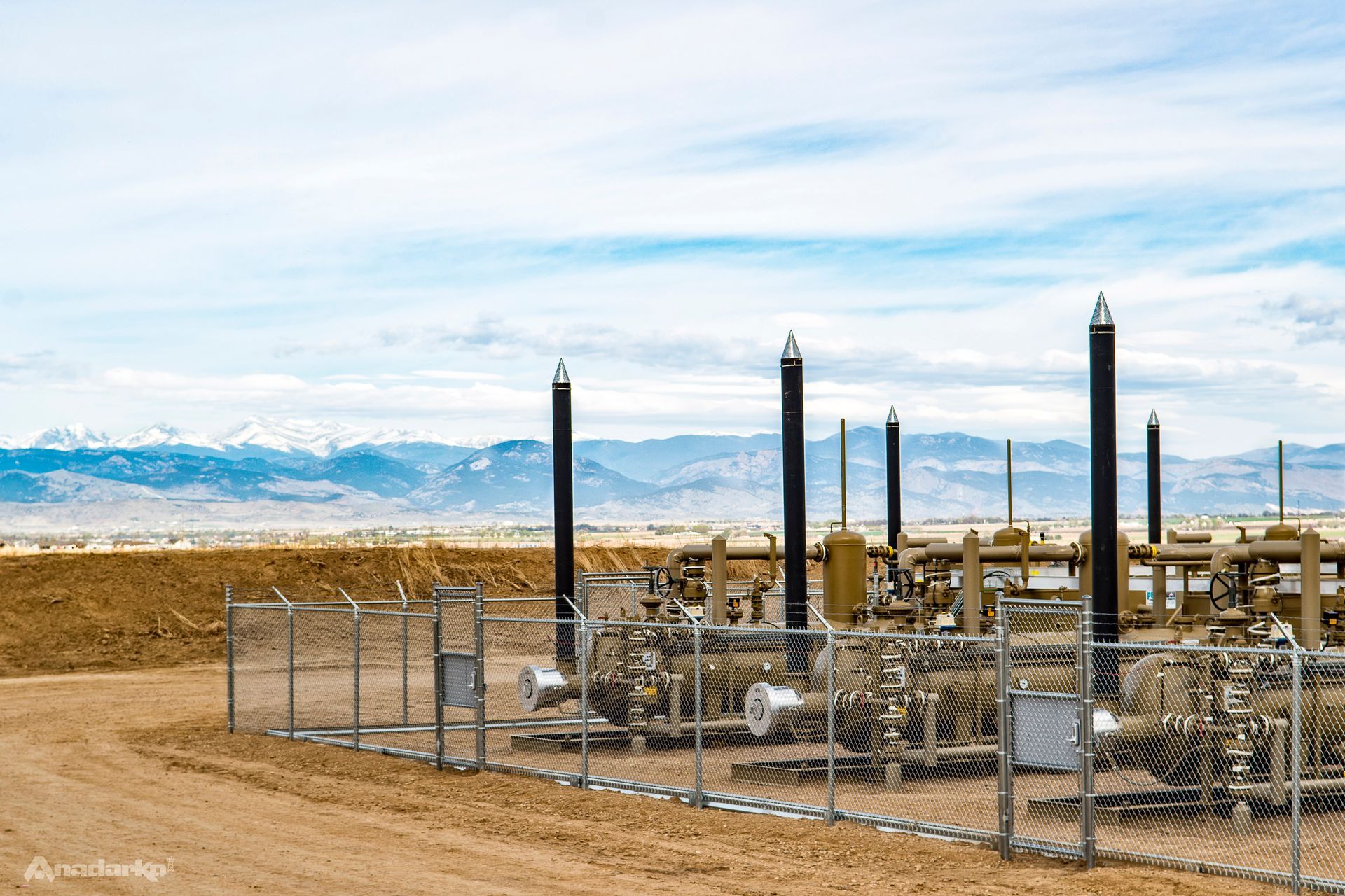 A fenced in area with a lot of pipes and mountains in the background.