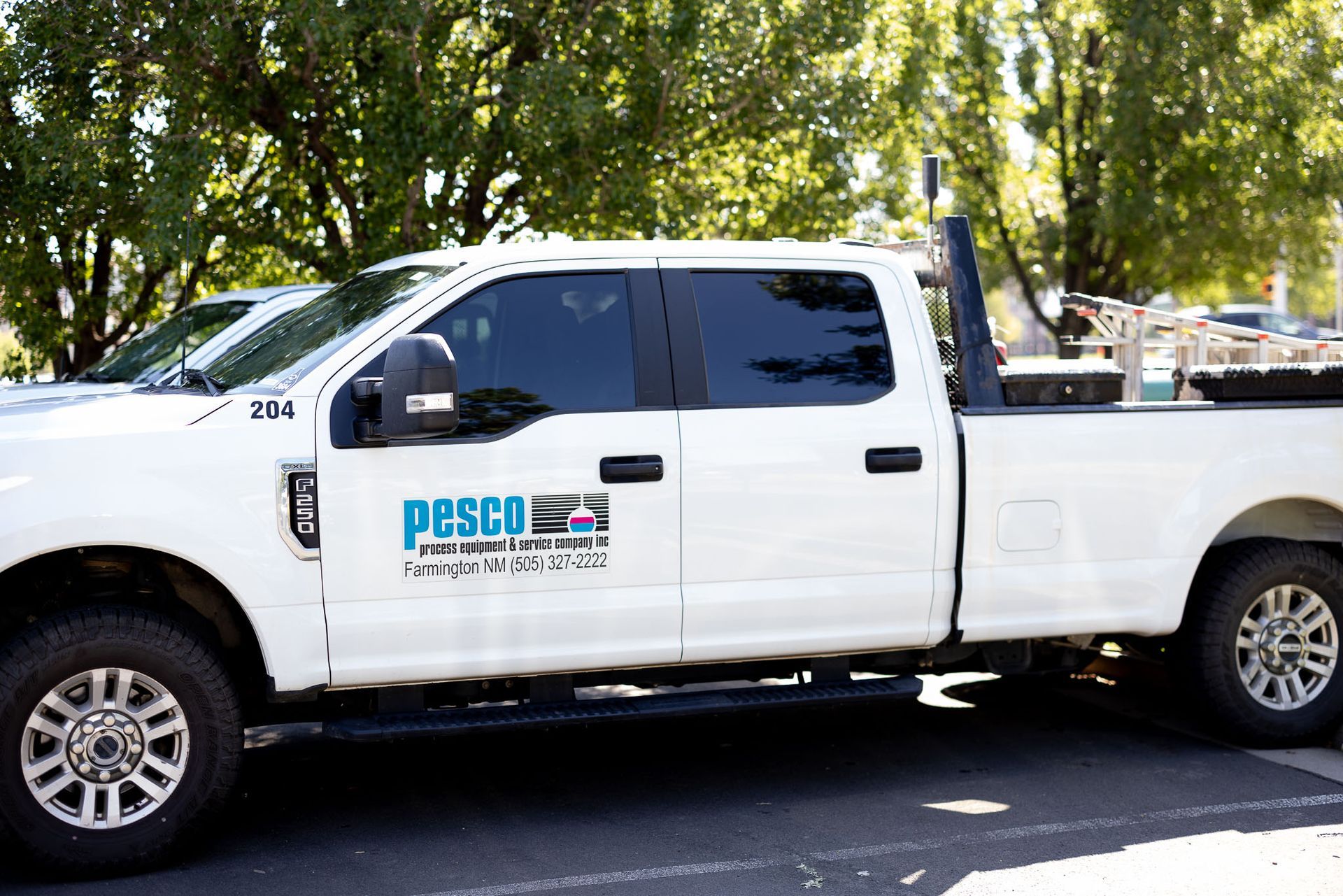 A white Pesco pickup truck is parked by some trees for the Denver Field Service team