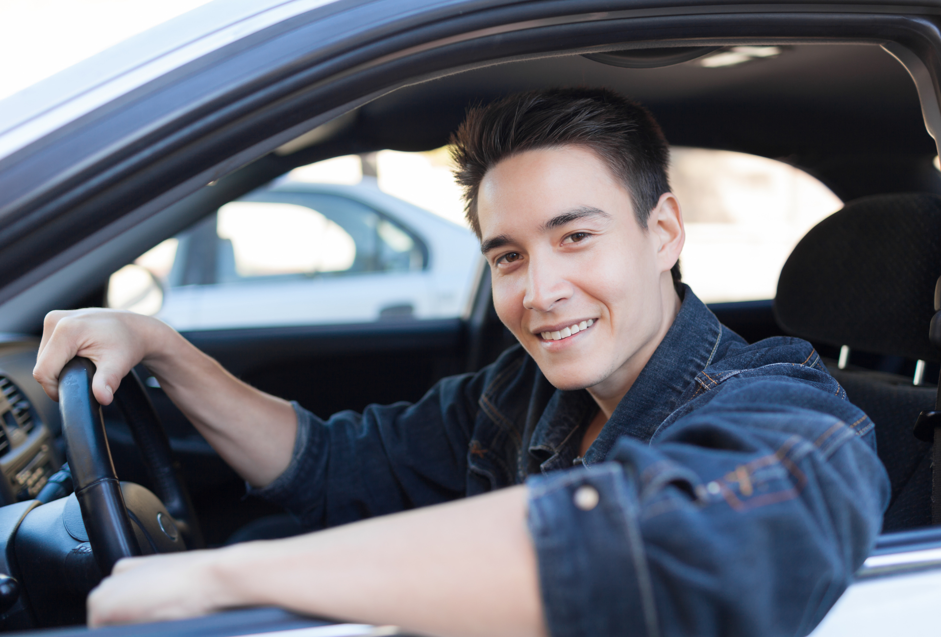Man smiles while driving a car, holding the steering wheel. Daylight, car interior.