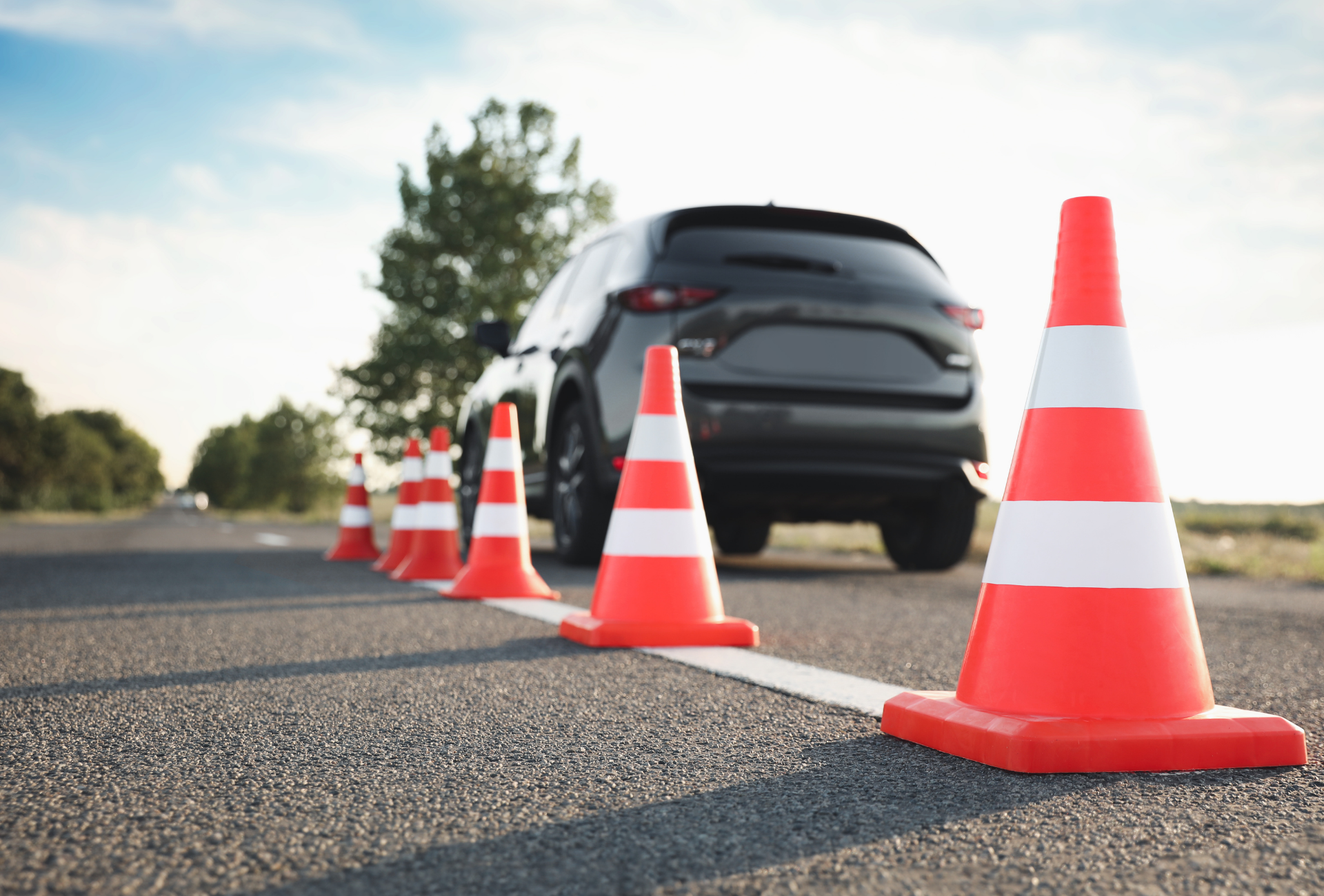 Orange traffic cones line a road; a dark SUV is in the background.