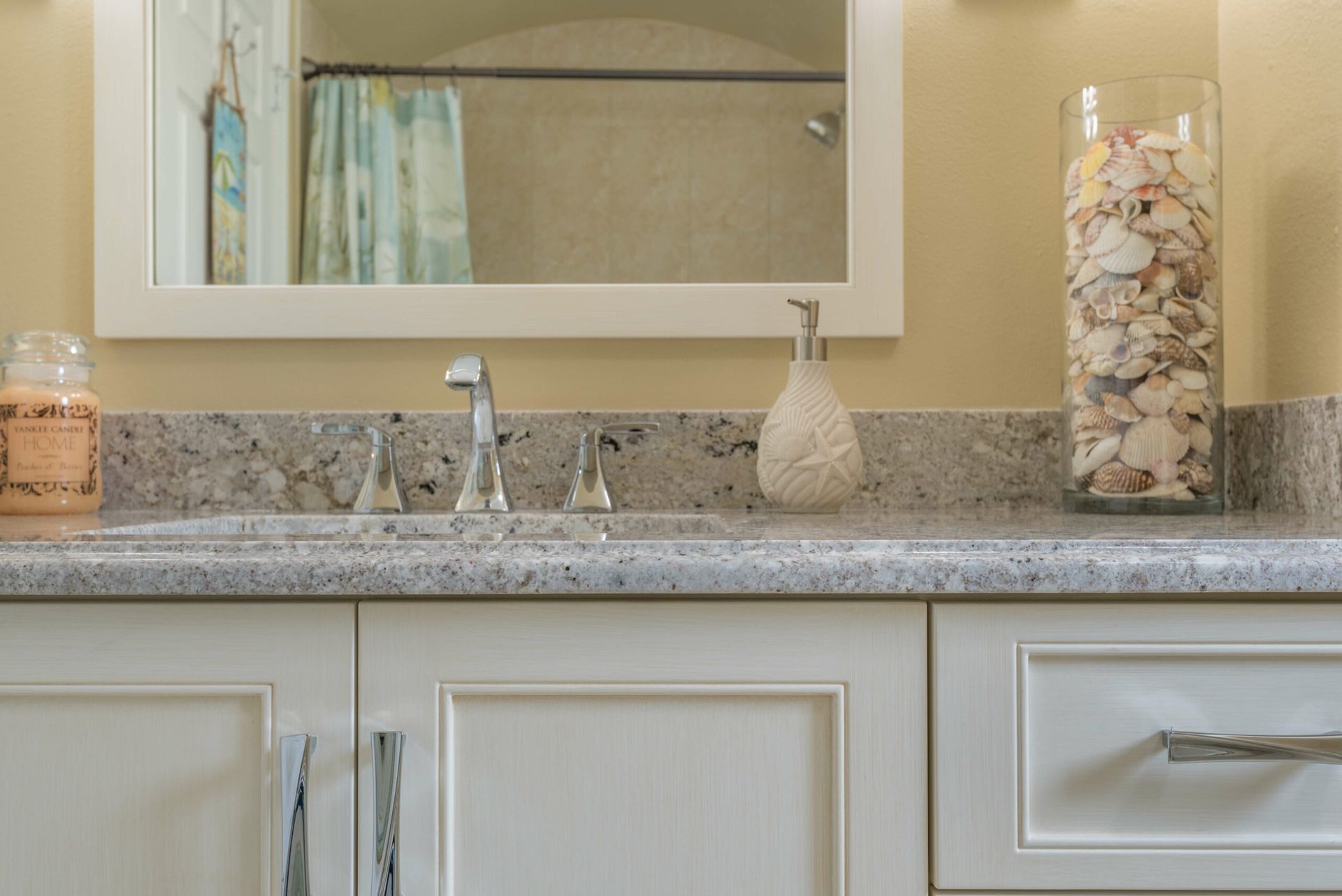 Bathroom vanity with granite countertop, sink, mirror, soap dispenser, and decorative jar of seashells