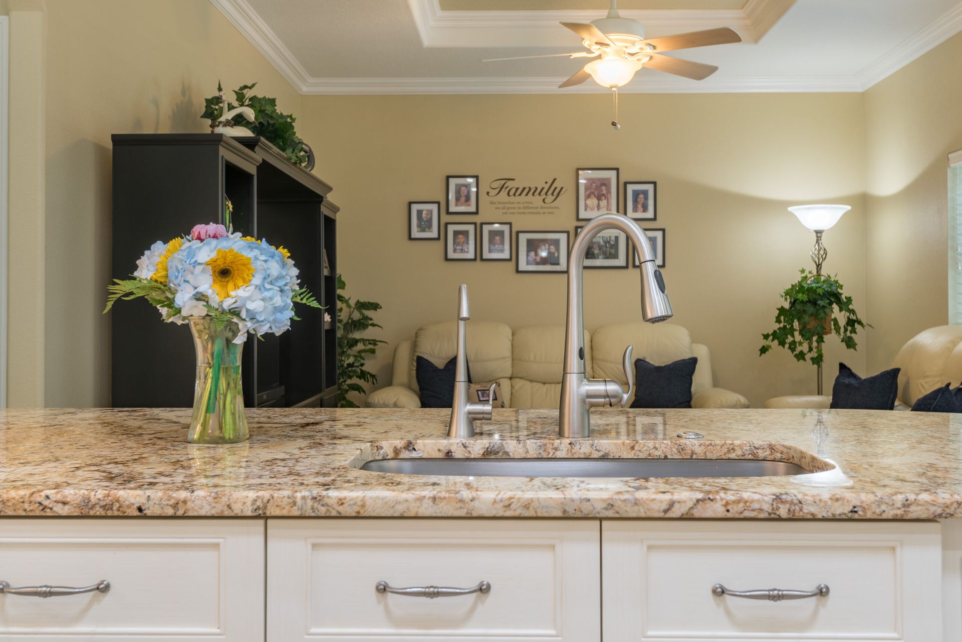 Kitchen island with granite countertop, vase of flowers, sink, and hanging light in a warmly lit home interior