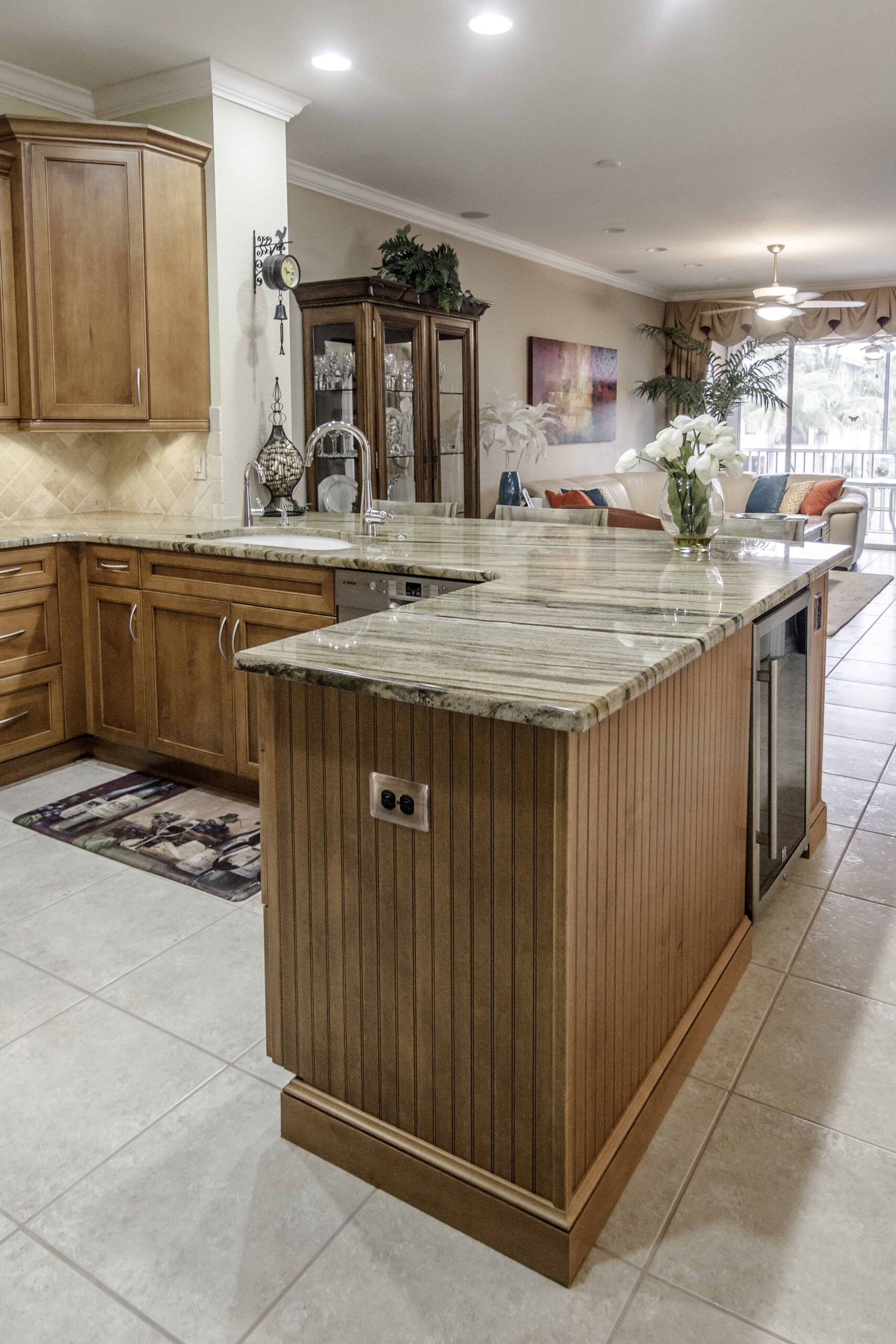 Bright kitchen with wood cabinets, granite island, tile floor, and decorative glass hutch.