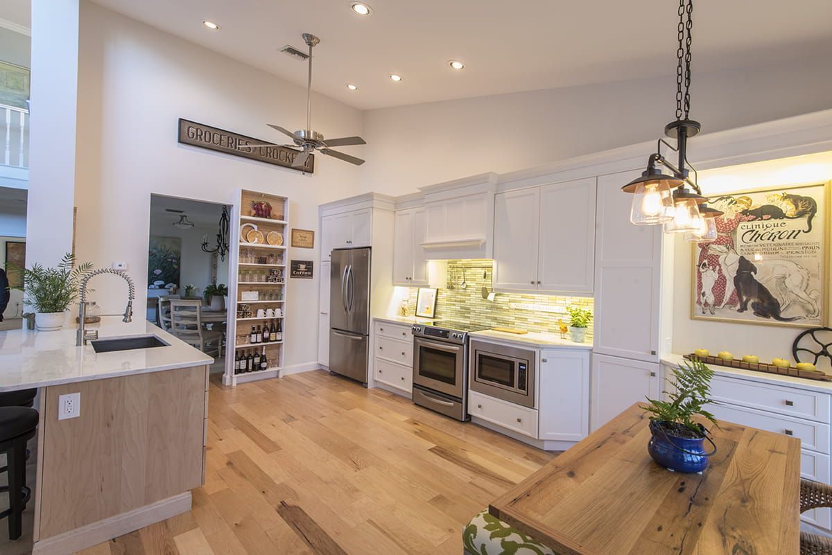 Bright modern kitchen with white cabinets, wood floors, island, and hanging pendant lights