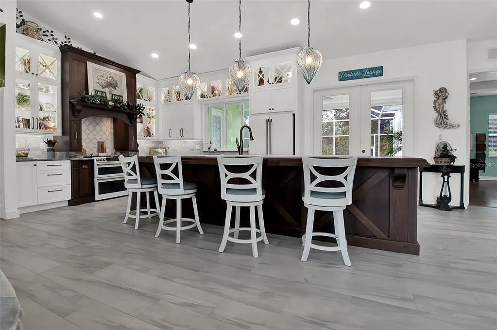 Modern kitchen with large island, white chairs, pendant lights, and gray wood flooring