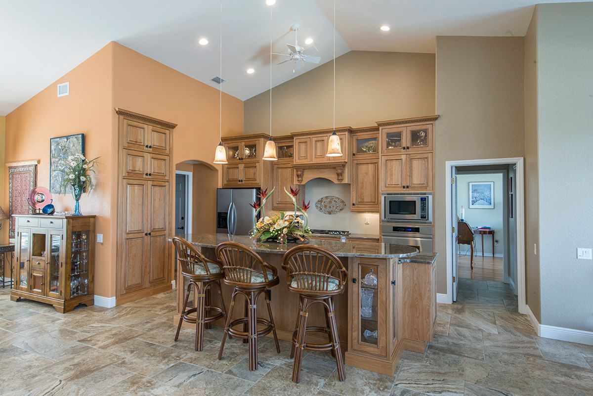 Spacious kitchen with wood cabinets, granite island, bar stools, and vaulted ceiling in a beige home