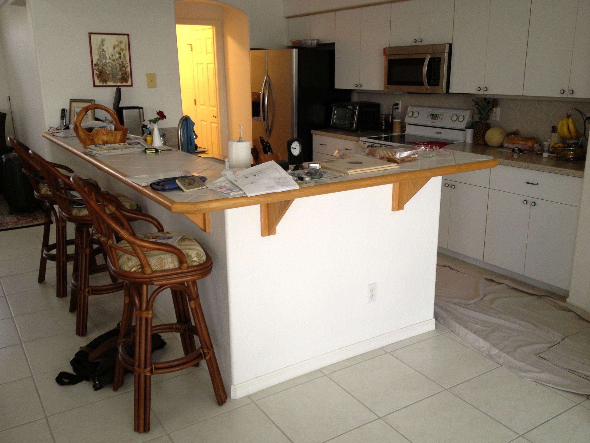 Kitchen with white cabinets, island counter, bar stools, and a doorway glowing with warm light.