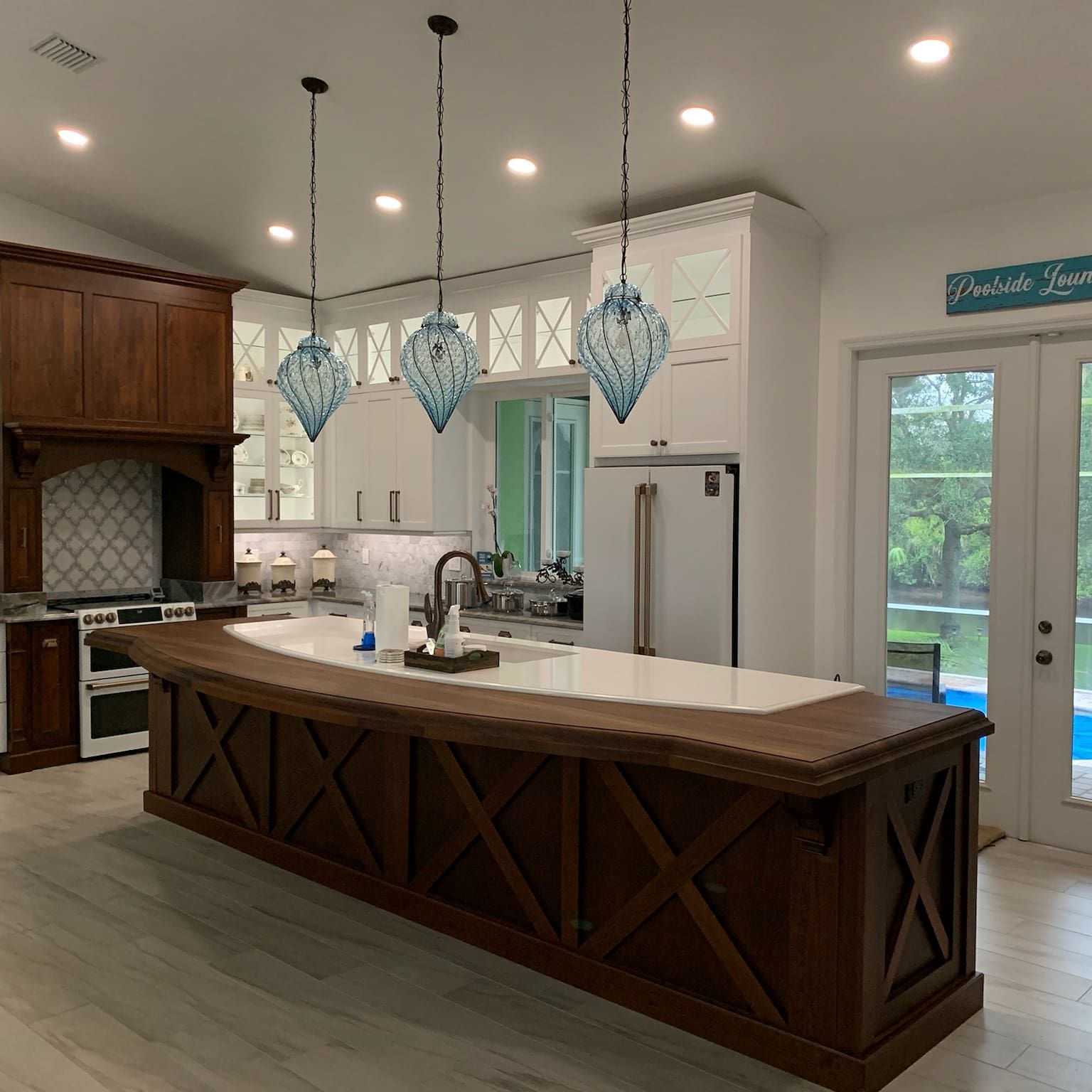 Kitchen design in Rotonda West, FL, modern kitchen with wood island, white cabinets, pendant lights, and large windows by patio doors