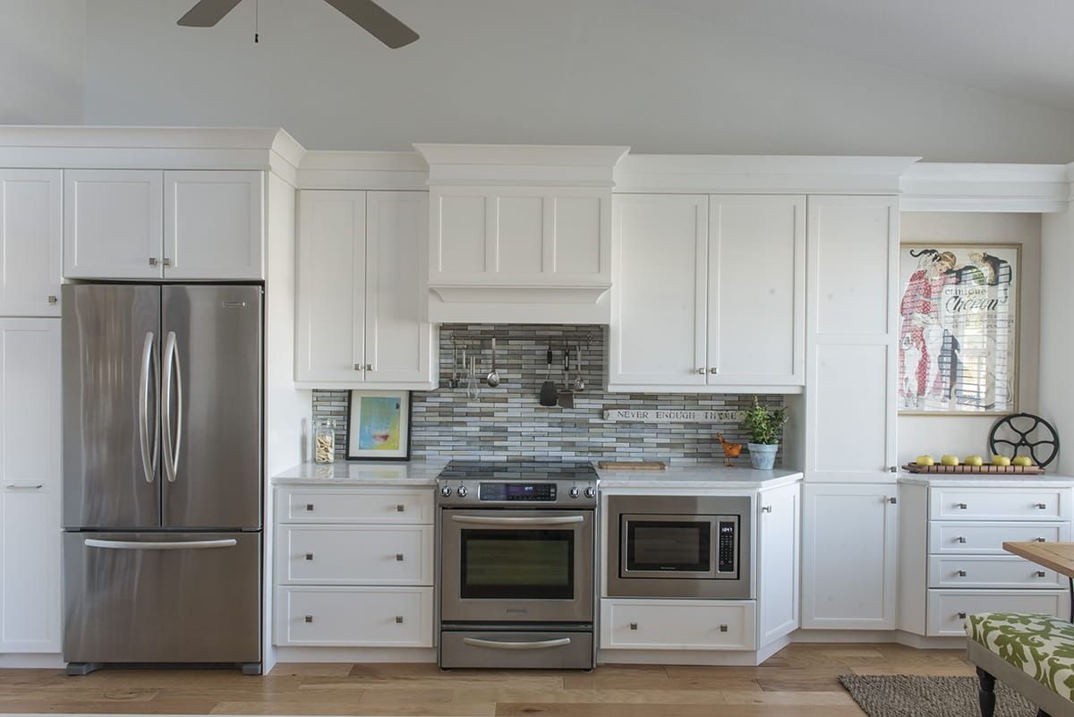 Modern white kitchen with stainless steel appliances, tiled backsplash, and window above the sink