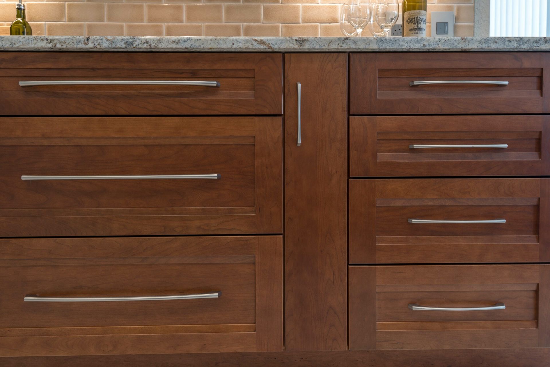 Dark wood kitchen cabinets with silver handles beneath a light countertop and tiled backsplash