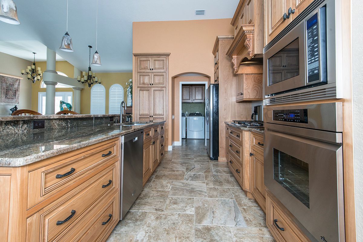 Modern kitchen with granite countertops, wood cabinets, and stainless steel appliances, viewed from the island.