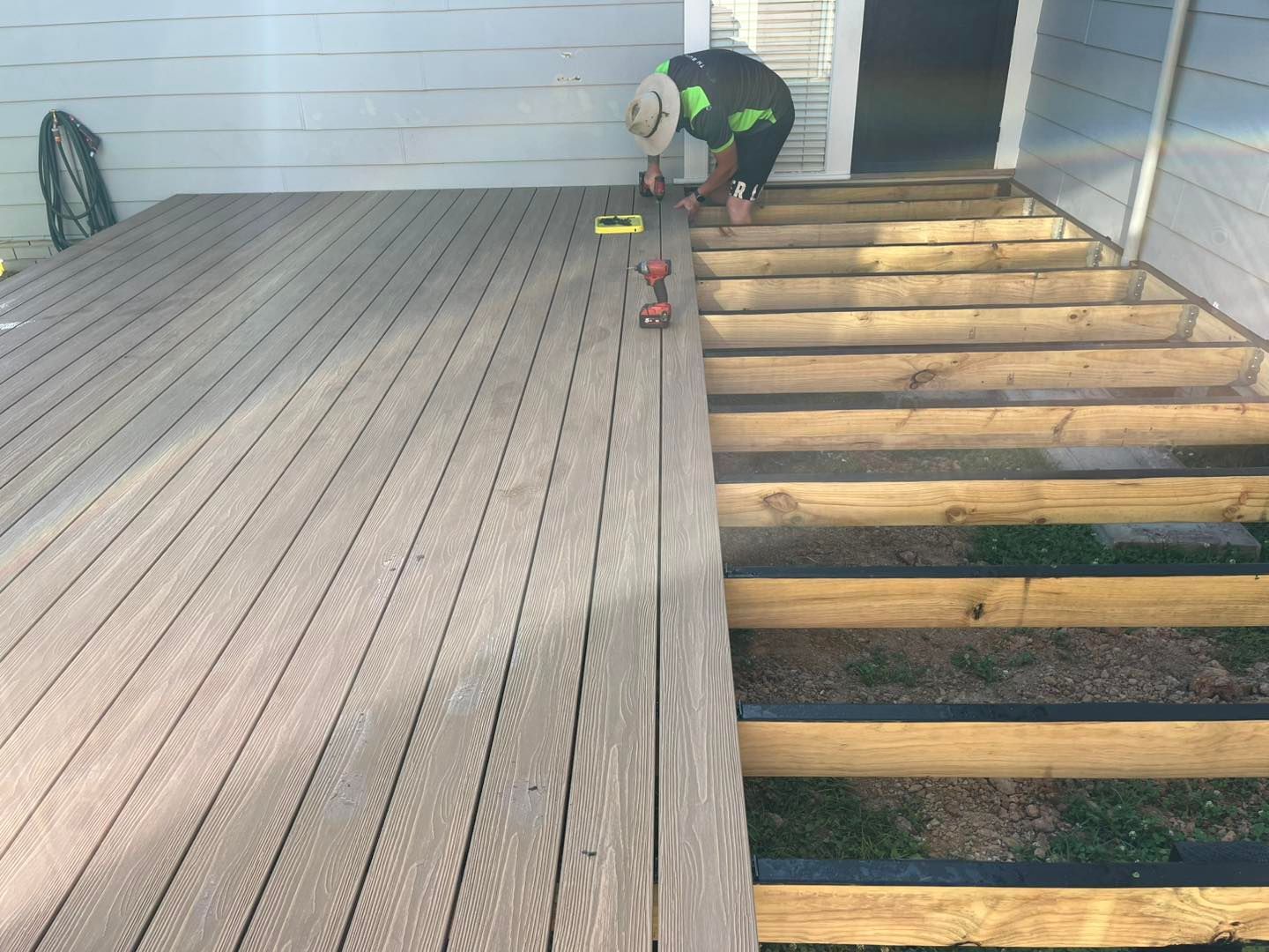 A Man is Installing a Wooden Deck With a Drill — TM Built Construction In Lochinvar, NSW