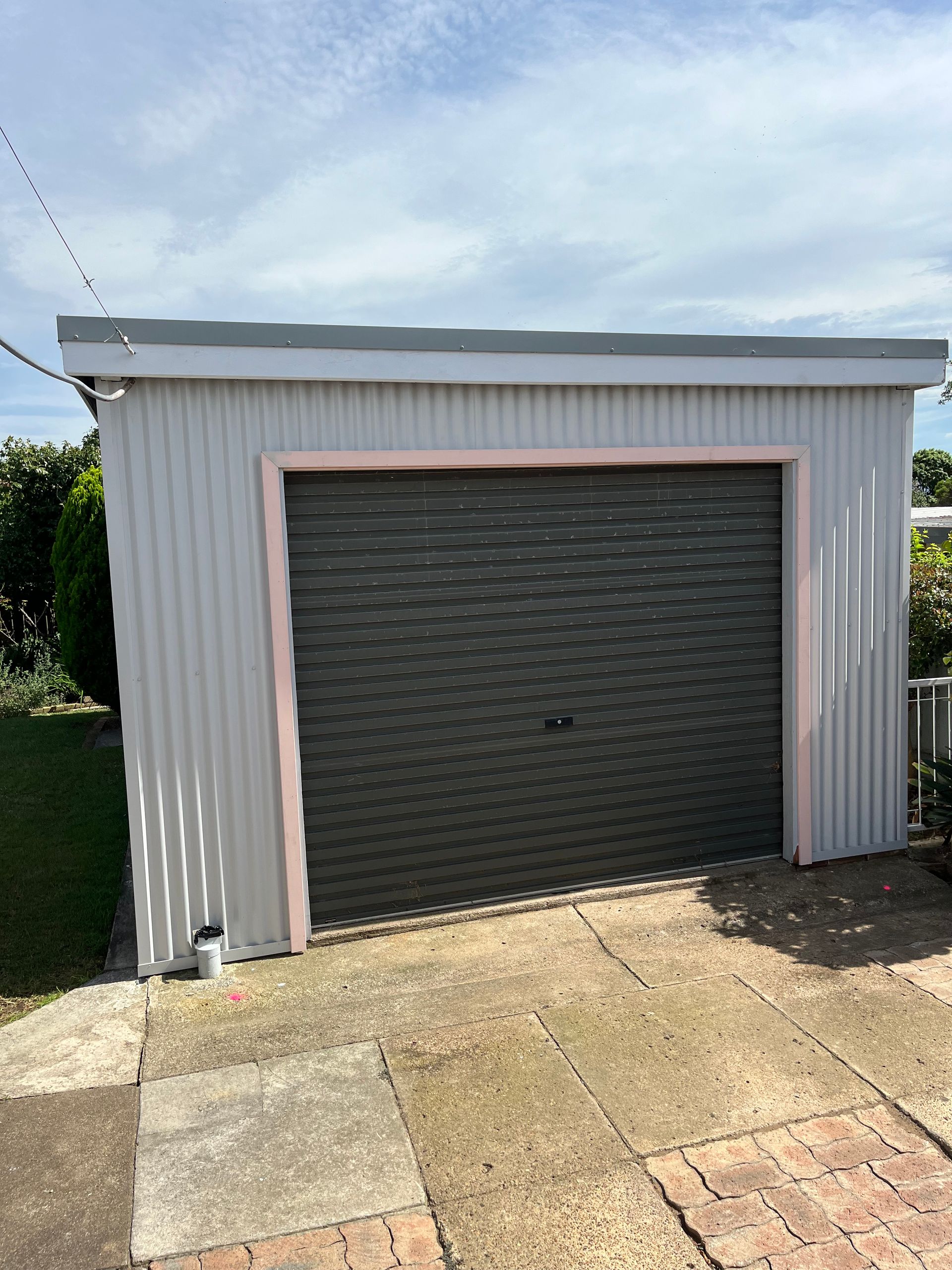 A white garage with a gray garage door is sitting on top of a brick driveway — TM Built Construction In Lochinvar, NSW