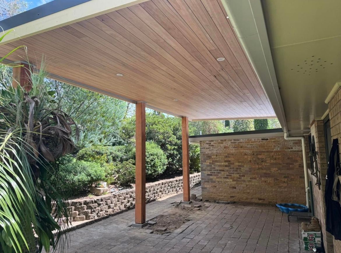 A patio with a wooden roof and a stone wall — TM Built Construction In Lochinvar, NSW