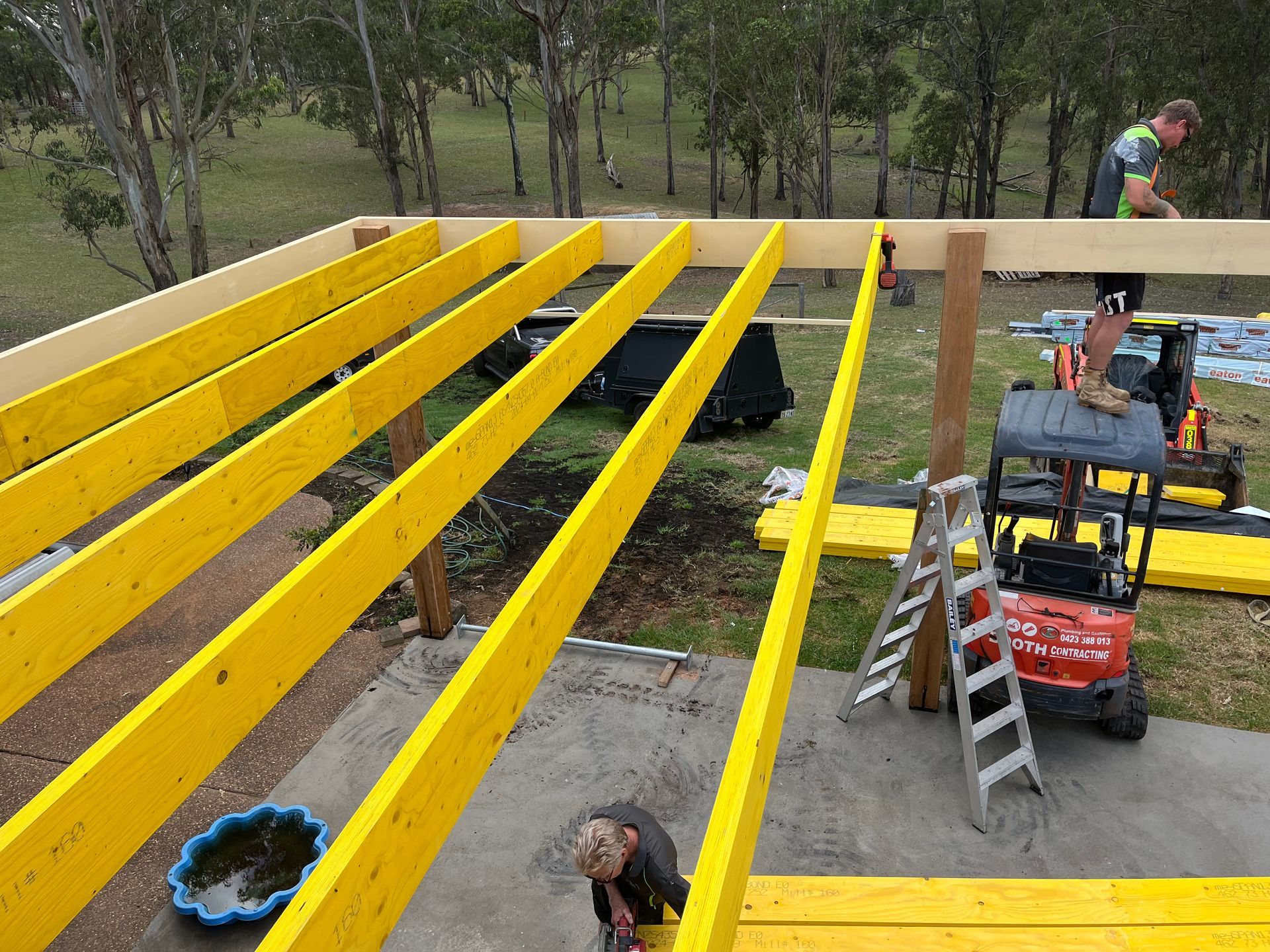 A man is working on a wooden structure with yellow beams — TM Built Construction In Lochinvar, NSW