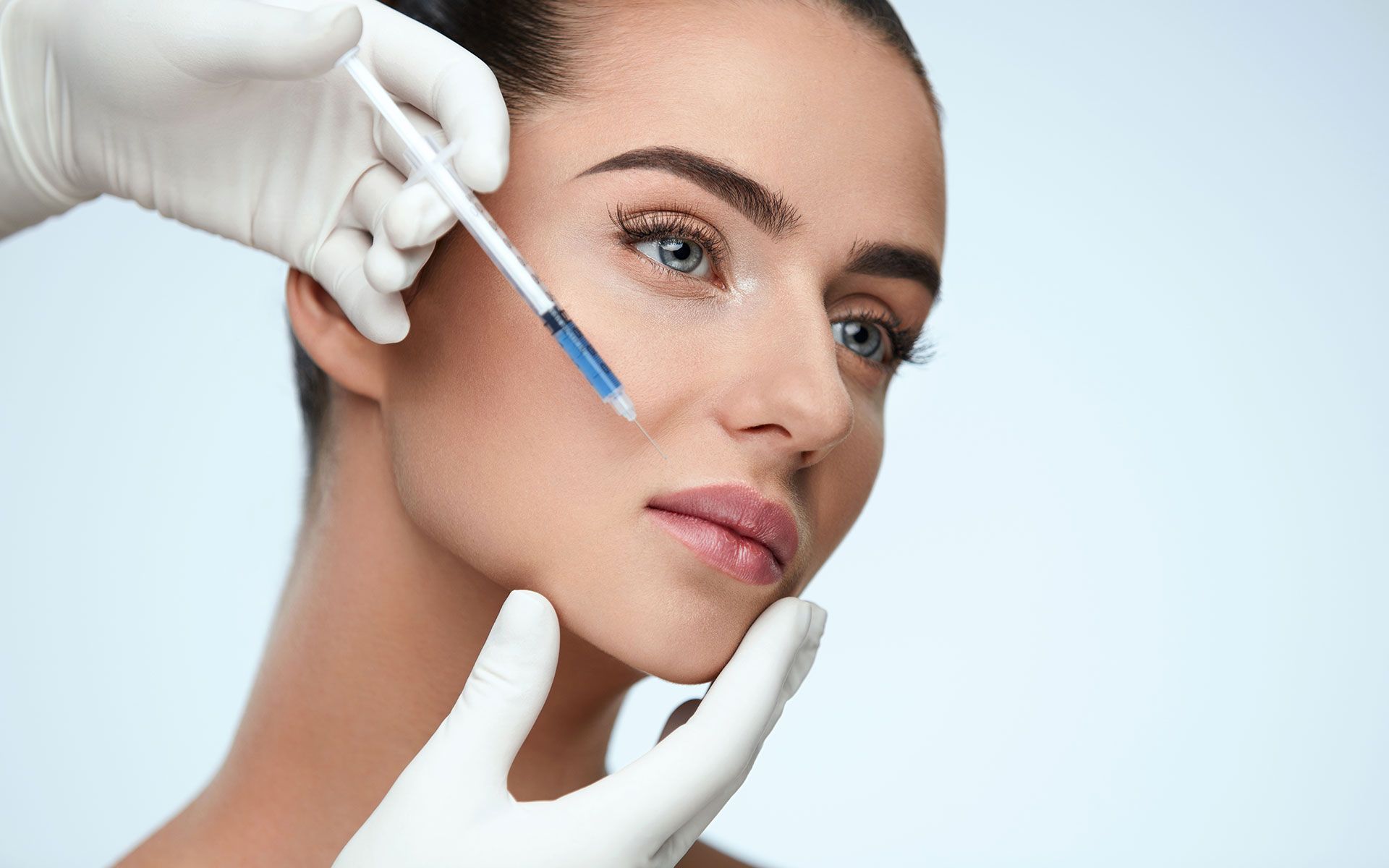 A woman getting a facial injection with a syringe, in a medical setting.