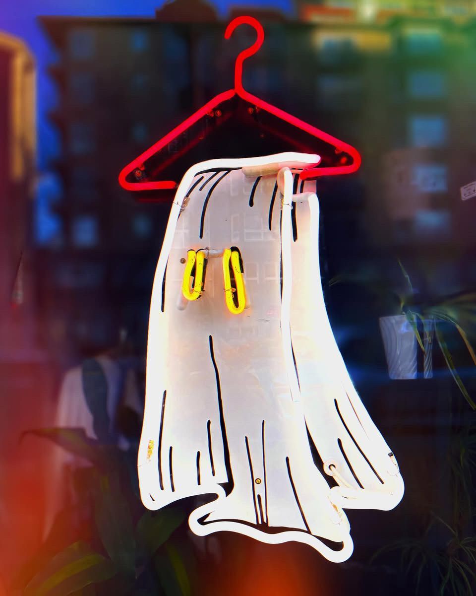 Neon sign by Yale Wolf of a ghost-shaped garment hanging on a red hanger. Yellow clips.