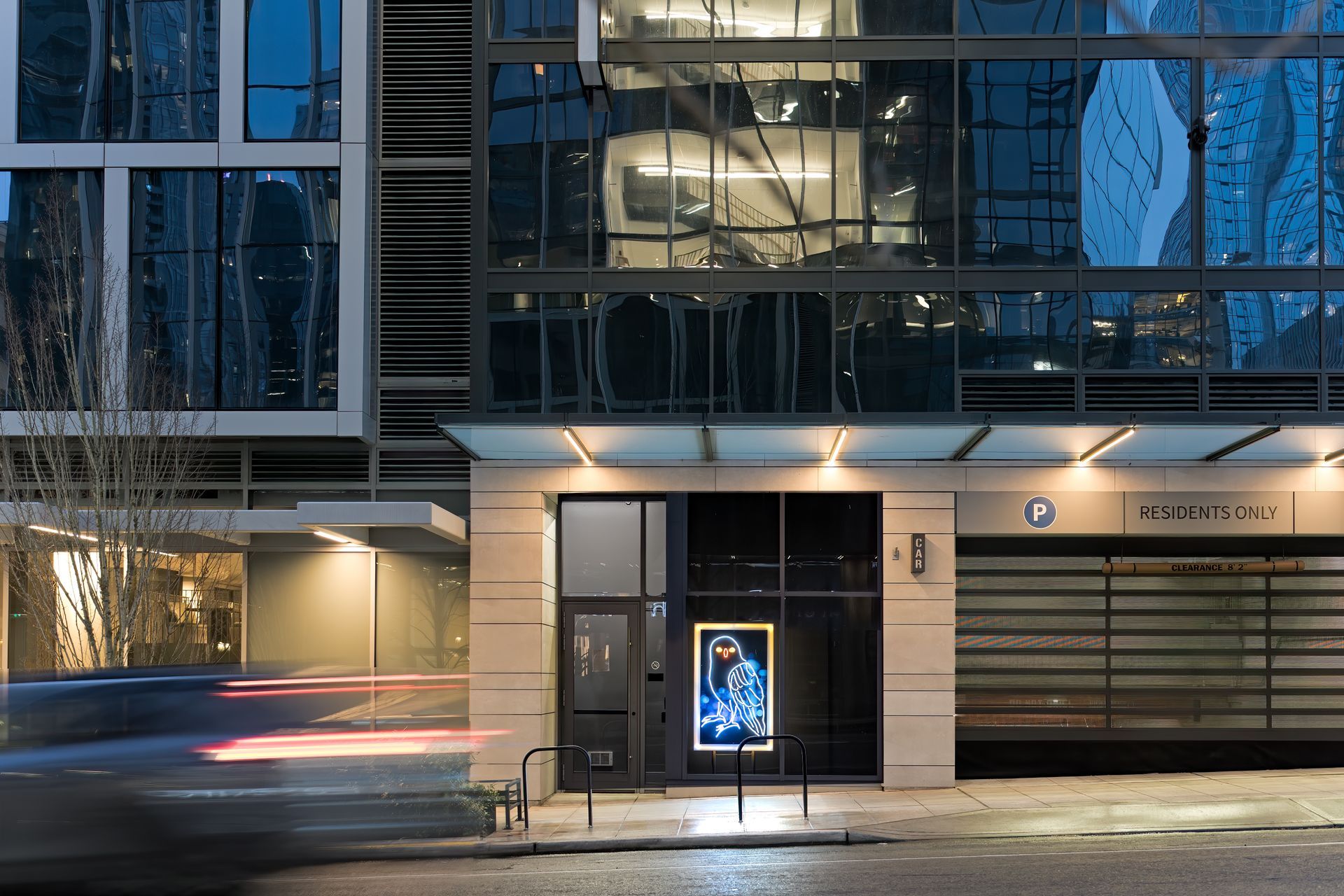 Night exterior of modern building with glass windows and lit entrance. Signage says 