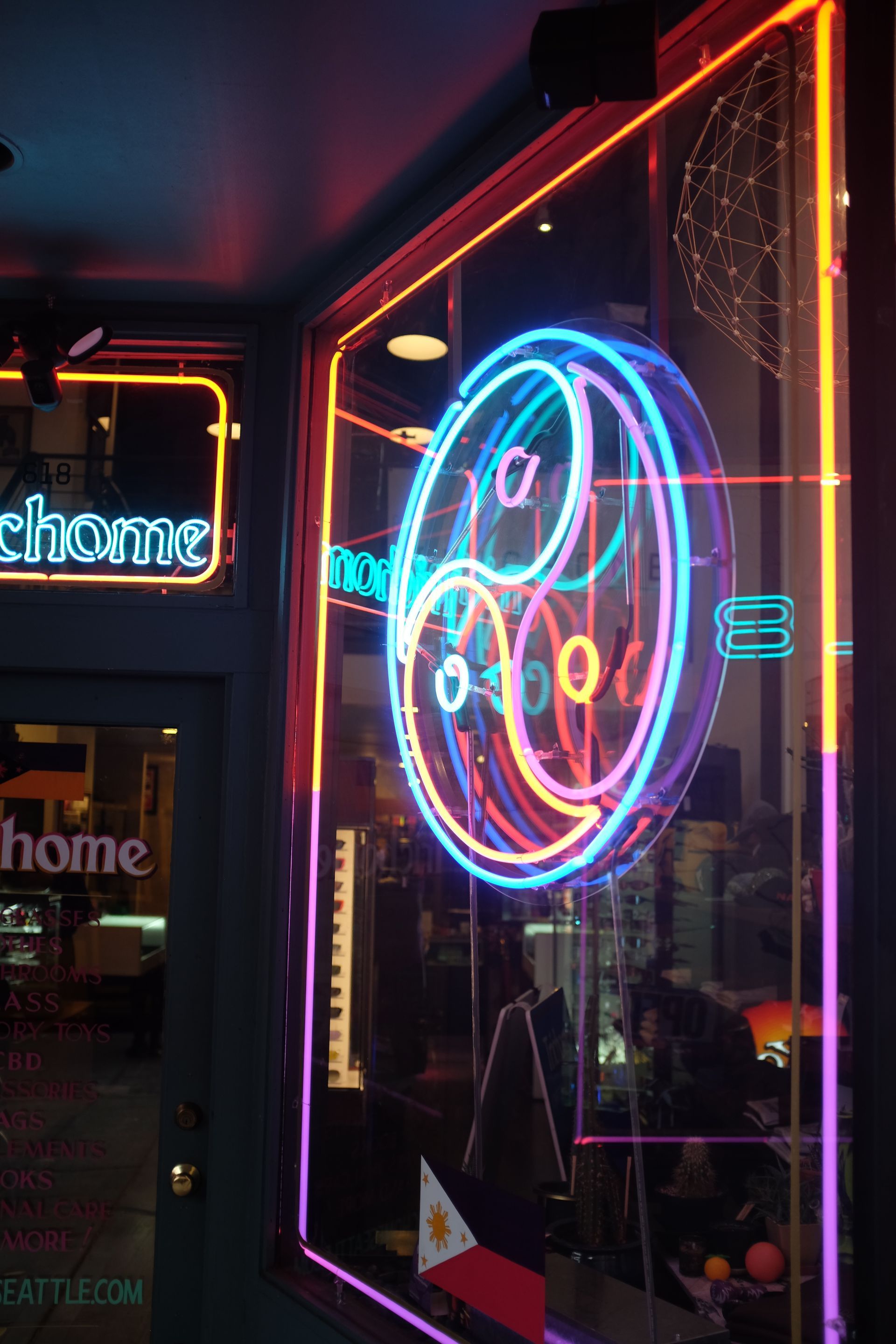 Neon sign by Yale Wolf with a yin and yang symbol in a shop window, framed in red and orange. 
