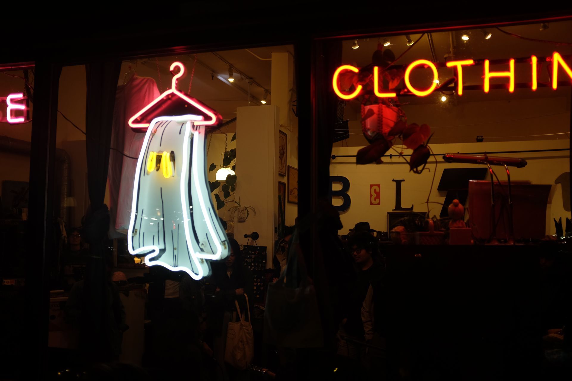 Neon clothing store window display with a ghost-shaped garment on a hanger; by Yale Wolf. 