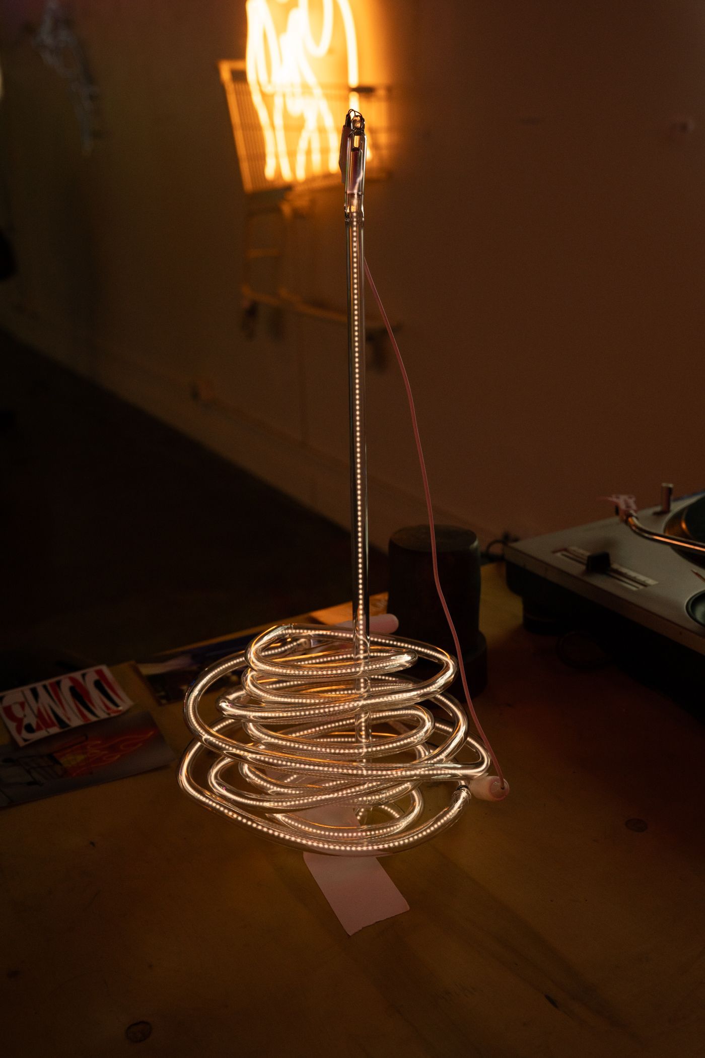 Coiled string lights illuminate a small desk, topped by a vertical light string with a flame at the top; art by Yale Wolf.
