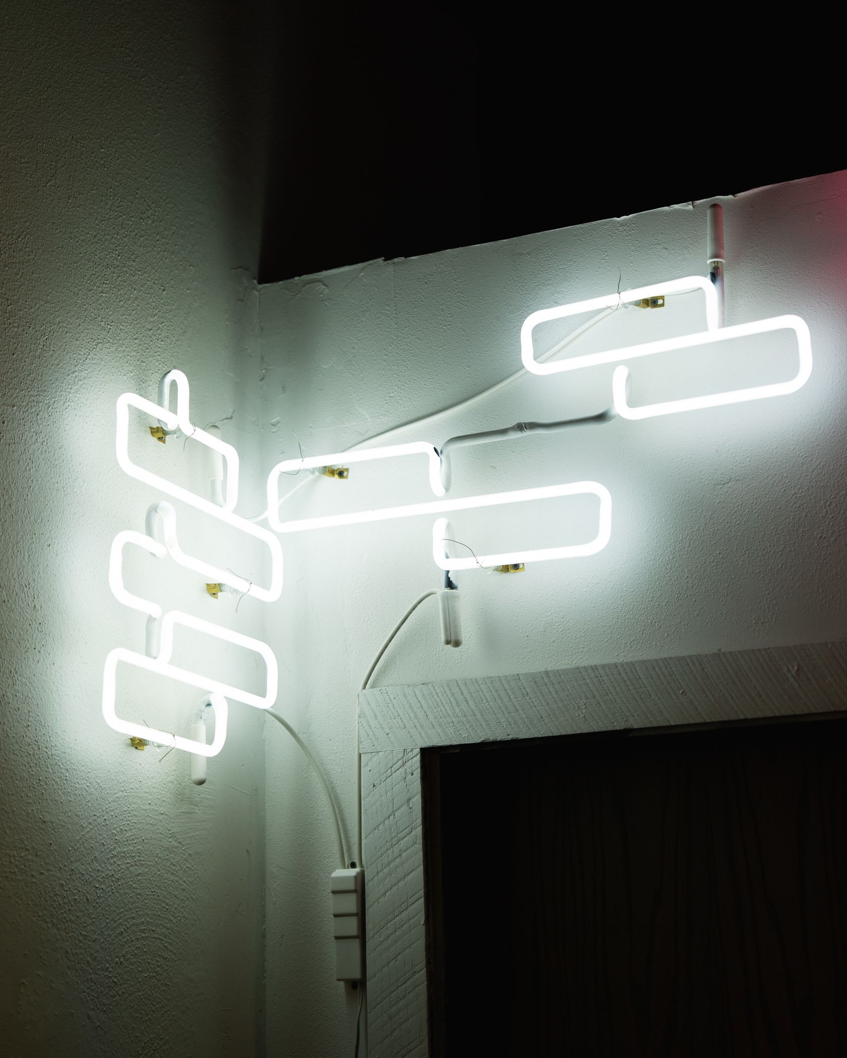 White neon light installation on a corner wall, composed of rectangular shapes and lines; art by Yale Wolf.