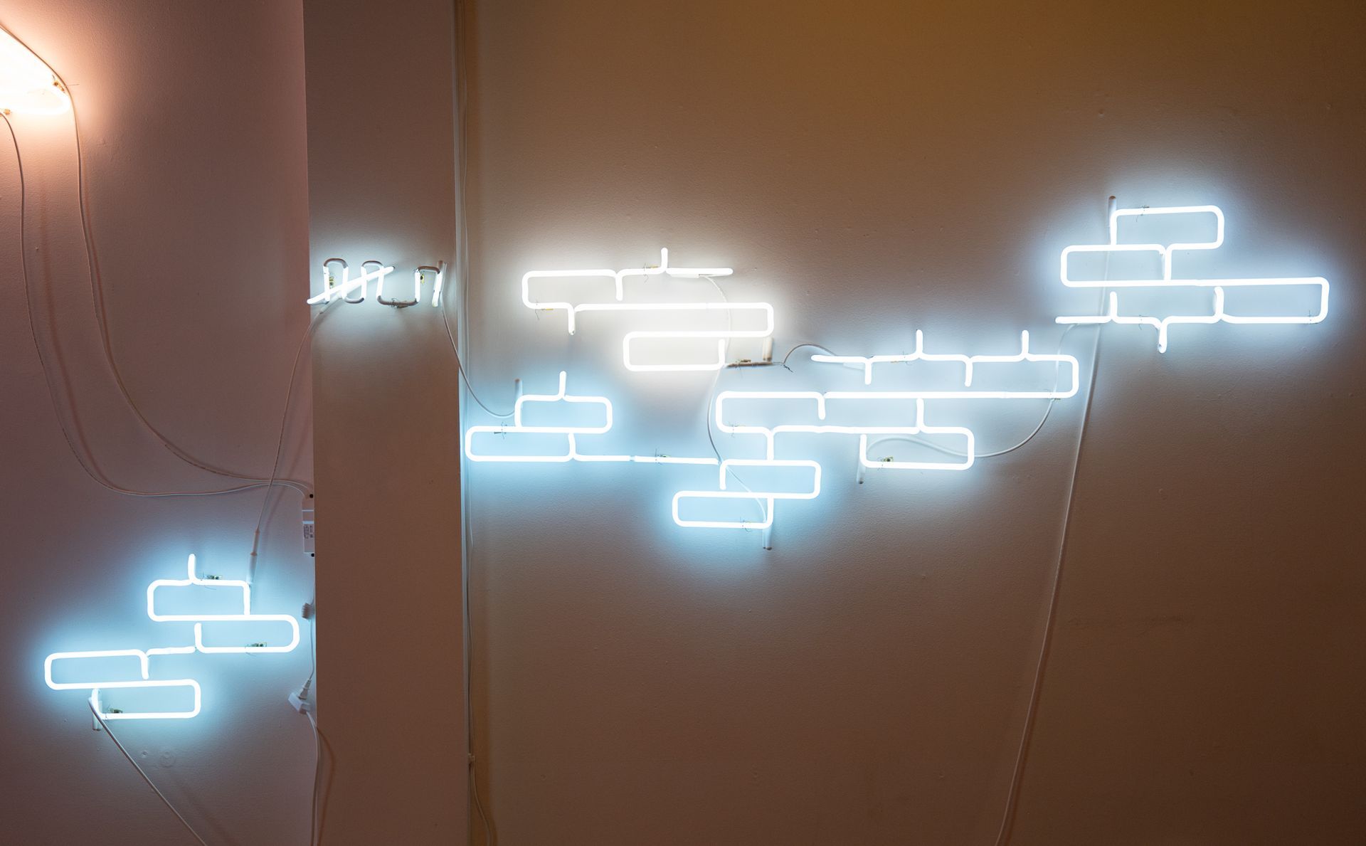 Blue neon light installation on a beige wall; depicts a brick pattern; art by Yale Wolf.