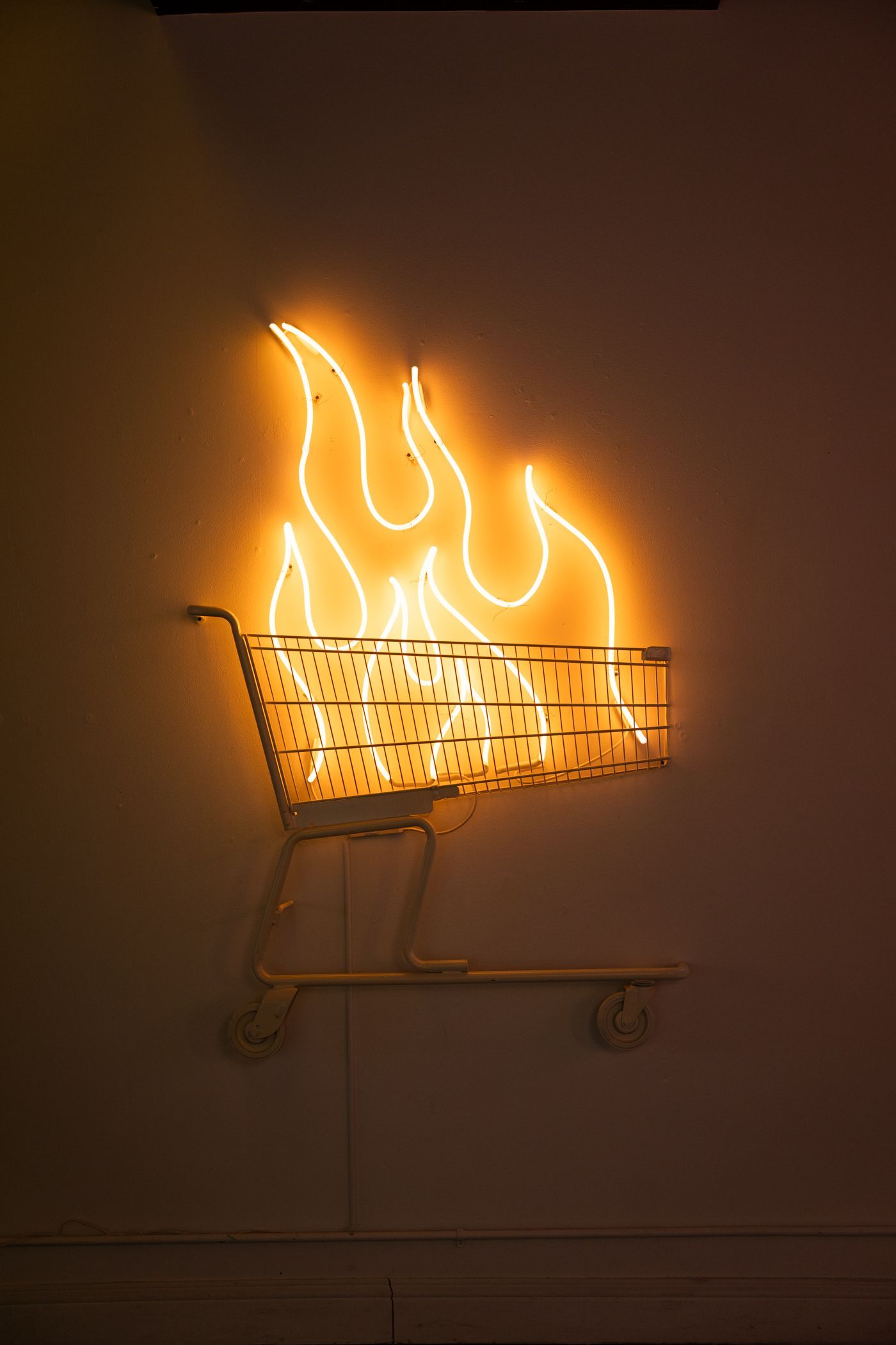 Neon sign: shopping cart engulfed in flames, glowing orange; art by Yale Wolf.