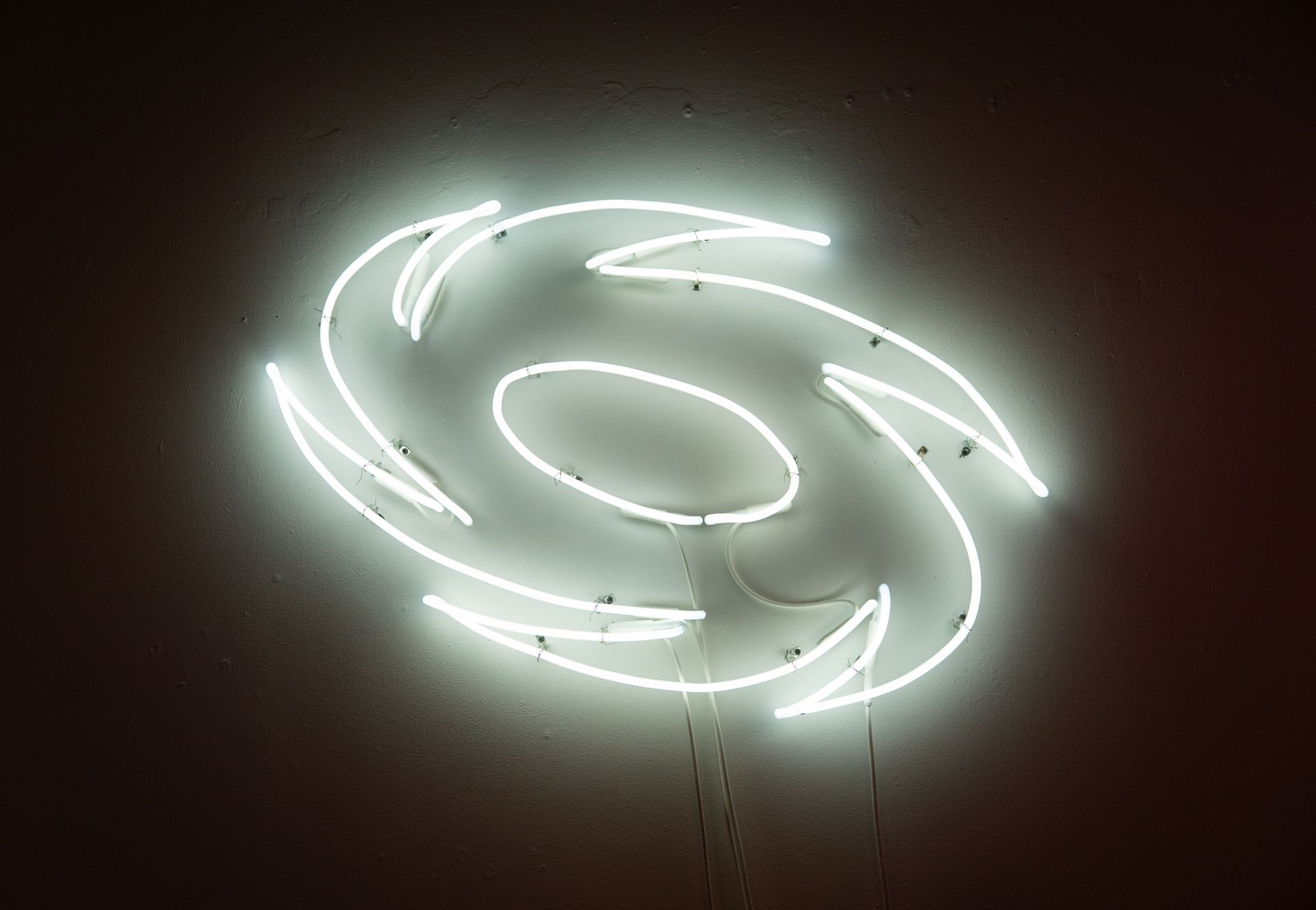 Neon white hurricane symbol on a dark wall; art by Yale Wolf.